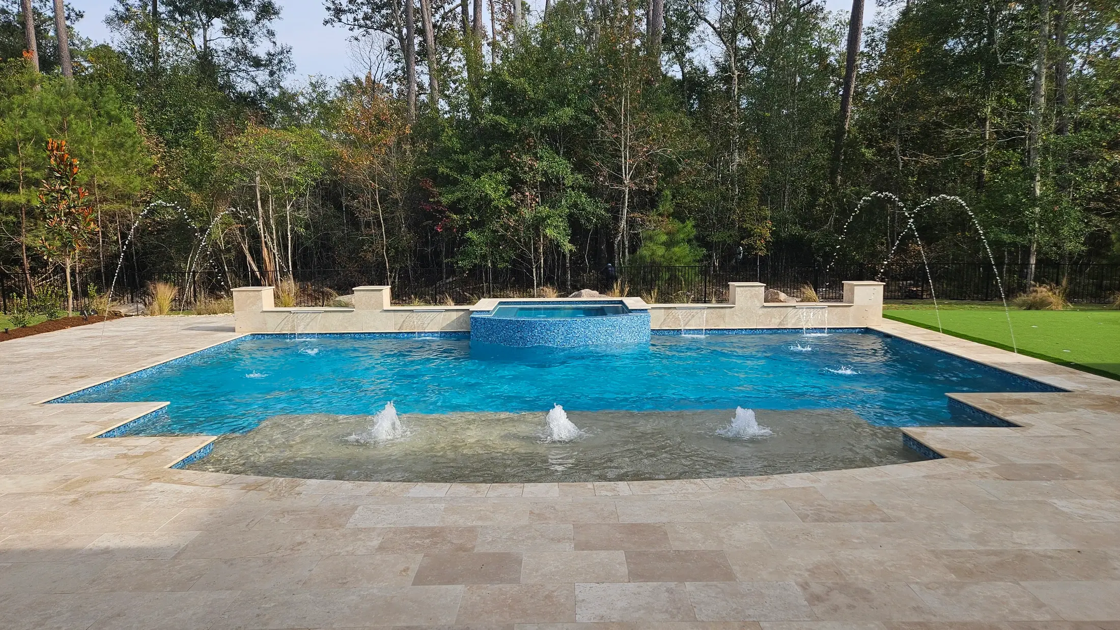 Clearwater custom pool with a broad tanning ledge, bubbler fountains, and a raised blue-tiled spa