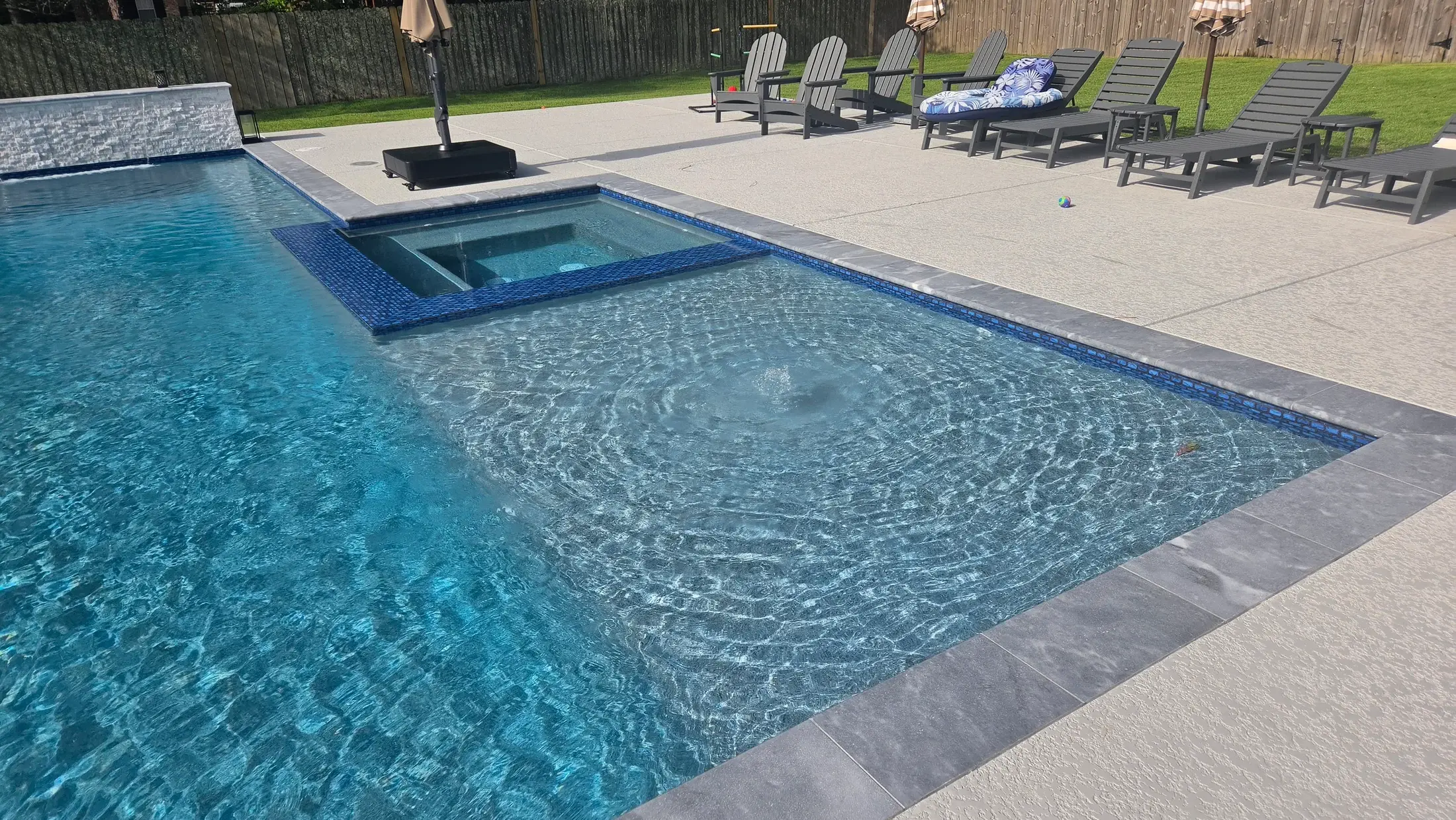 Clearwater integrated blue-tiled spa beside a swimming pool and terrace with lounge chairs